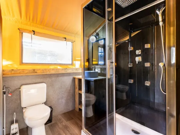 Das Badezimmer des Roan Lodgetent Premium XL verfügt über eine luxuriöse Duschkabine, eine Toilette und ein Waschbecken.