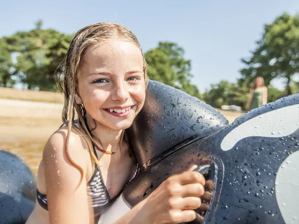 Mädchen mit aufblasbarem Spielzeug in einem natürlichen See auf dem Roan Camping De Schatberg.