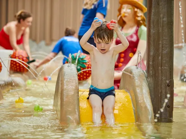 Kleiner Junge hat Wasserspaß von der Rutsche im Planschbecken auf dem Roan Camping Terspegelt.