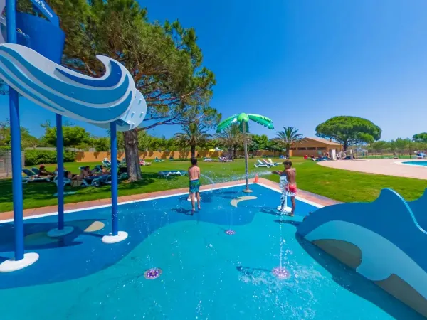 Sprühpark und Liegewiese mit Sonnenliegen im Schatten auf dem Campingplatz Roan Platja Brava.