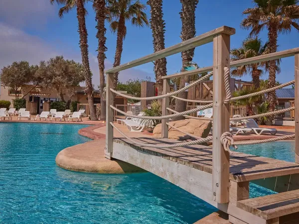 Brücke und Liegestühle am Pool des Campingplatzes Le Petit Mousse in Roan.