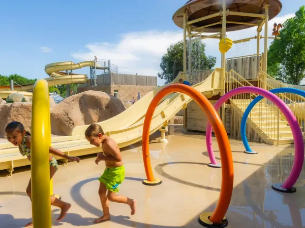 Kinder rennen durch die Wassersprinkler auf dem Roan-Campingplatz Arinella Bianca.